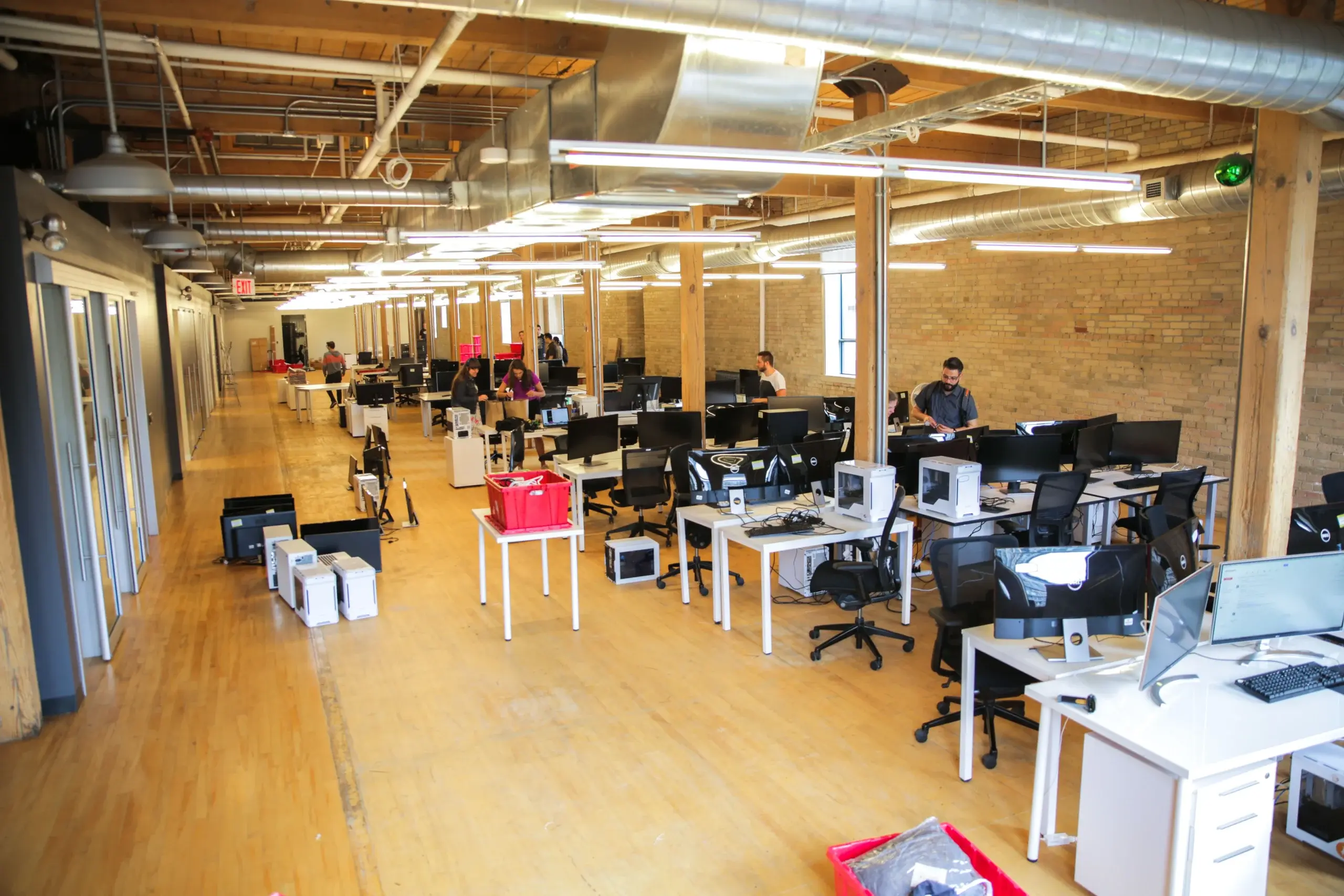Open coworking office with rows of desks, computer monitors, and staff working under bright ceiling lights, reflecting technology recruitment.