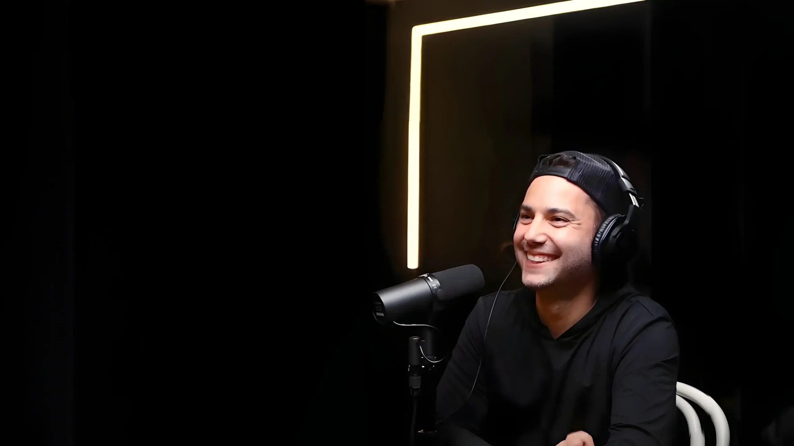 Smiling recruiter in headphones speaks into a studio microphone, with a glowing light panel in the background.