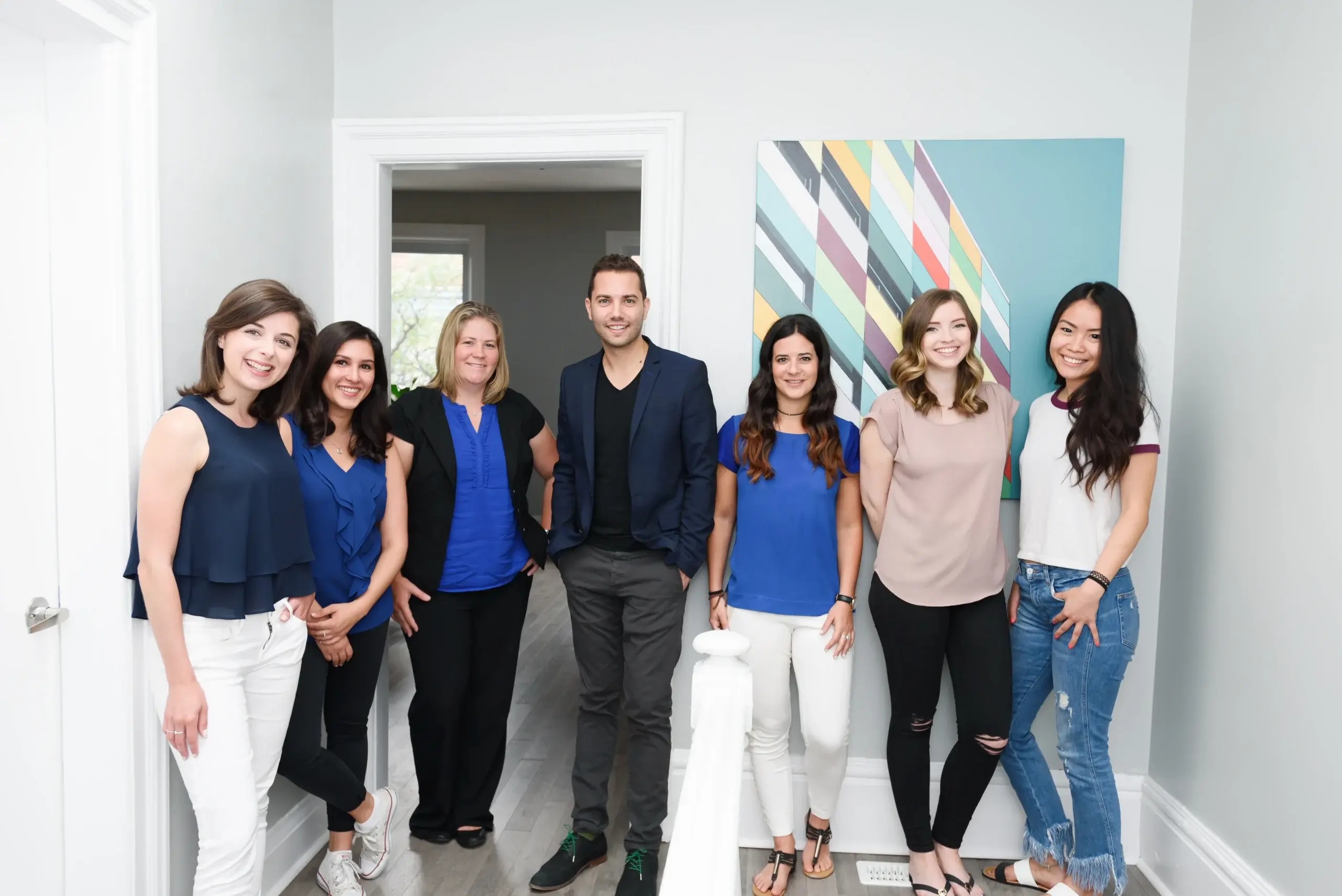 Six professionals pose in a bright office doorway, smiling. Diverse recruitment and employer branding for recruitment are reflected in the welcoming team culture.