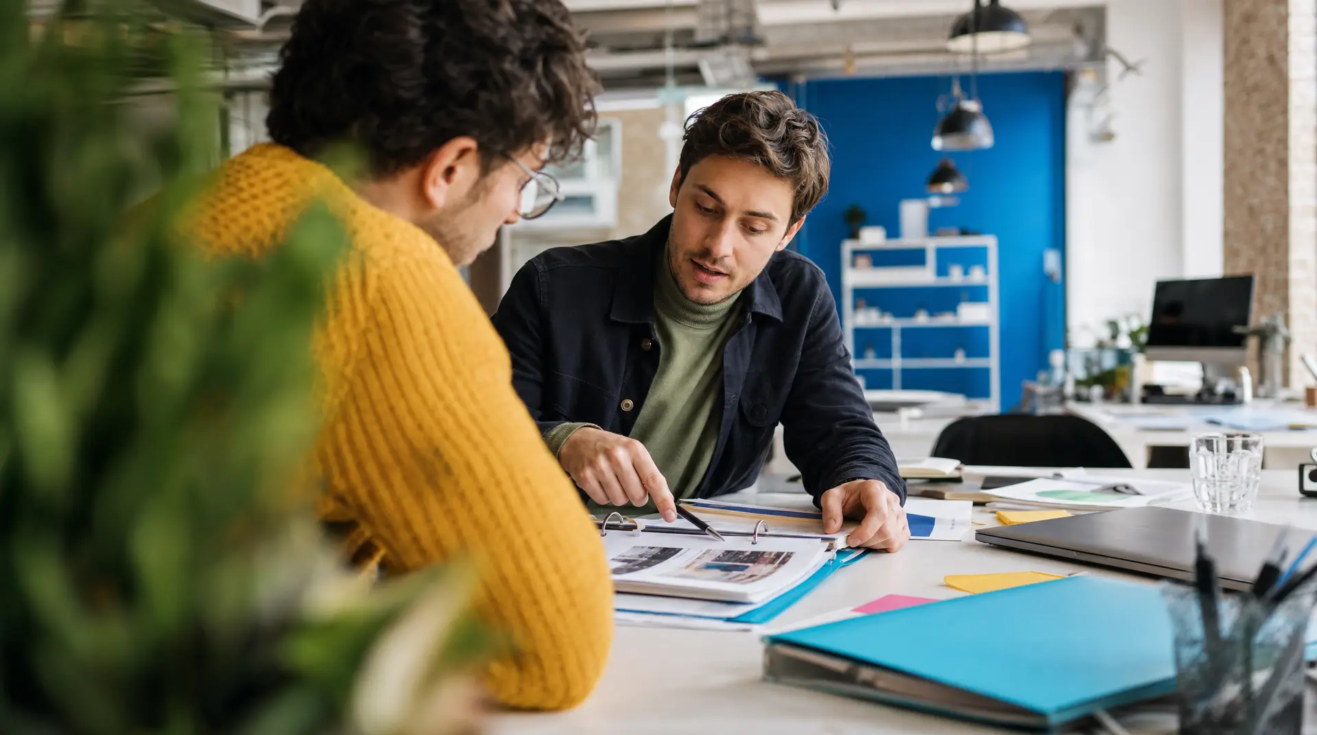 Two people collaborate over printed documents at a desk in a modern office, aligning on the recruitment process and next steps.