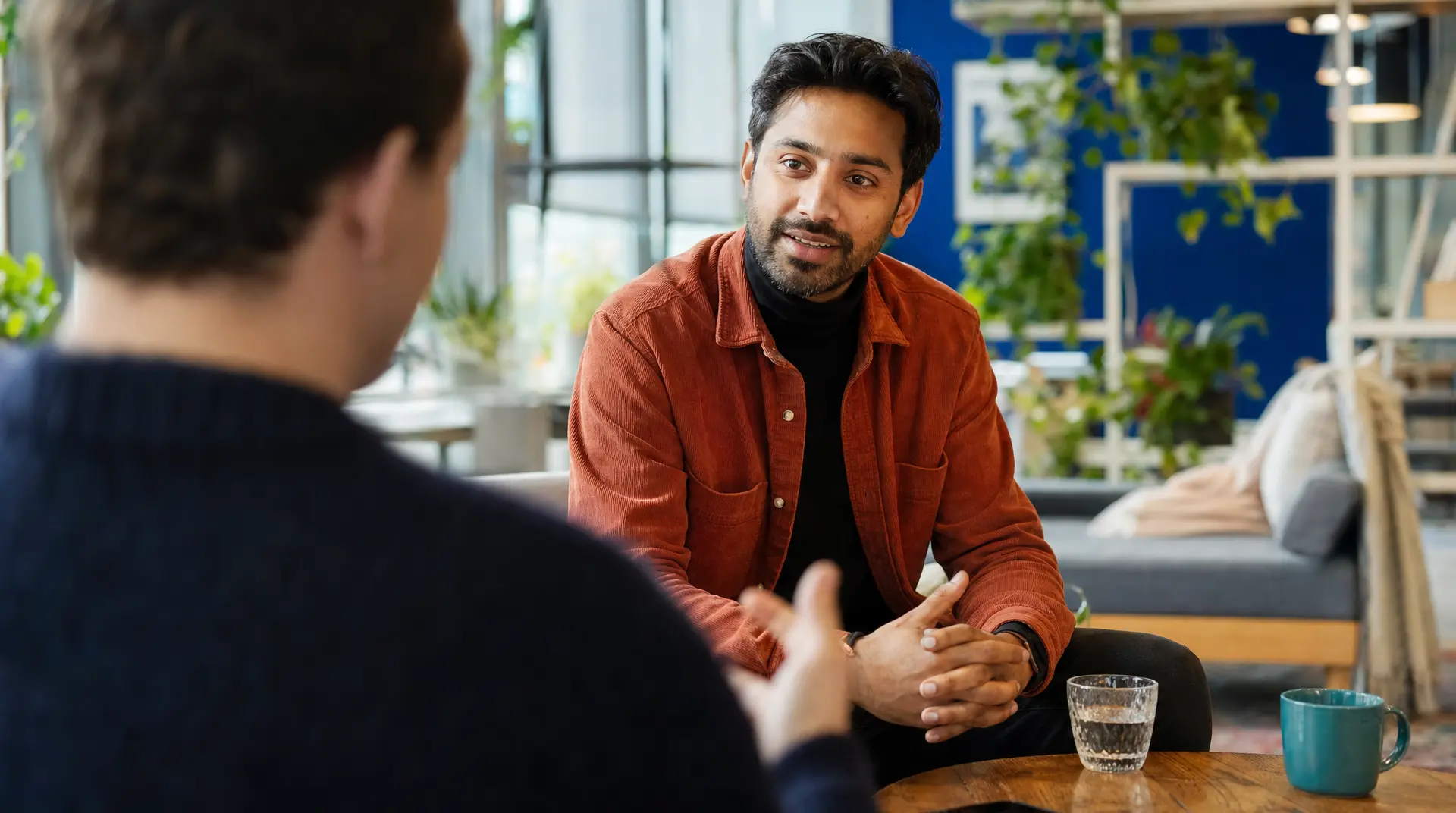 Two people meet across a table in a modern office, as the interviewer discusses the recruitment process with a job candidate.