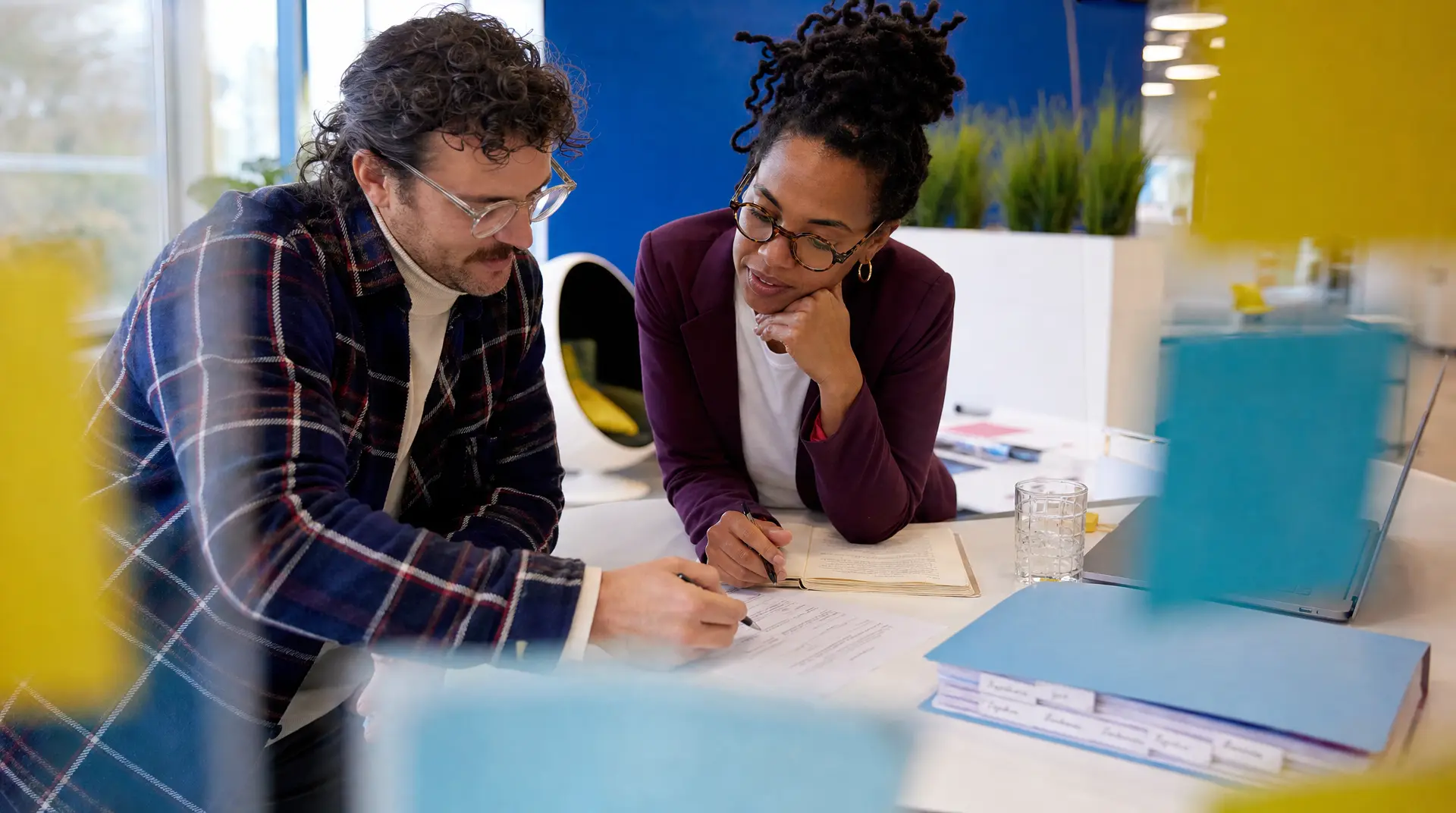 Two recruiters review paperwork at a shared desk, laptops open during talent acquisition interview