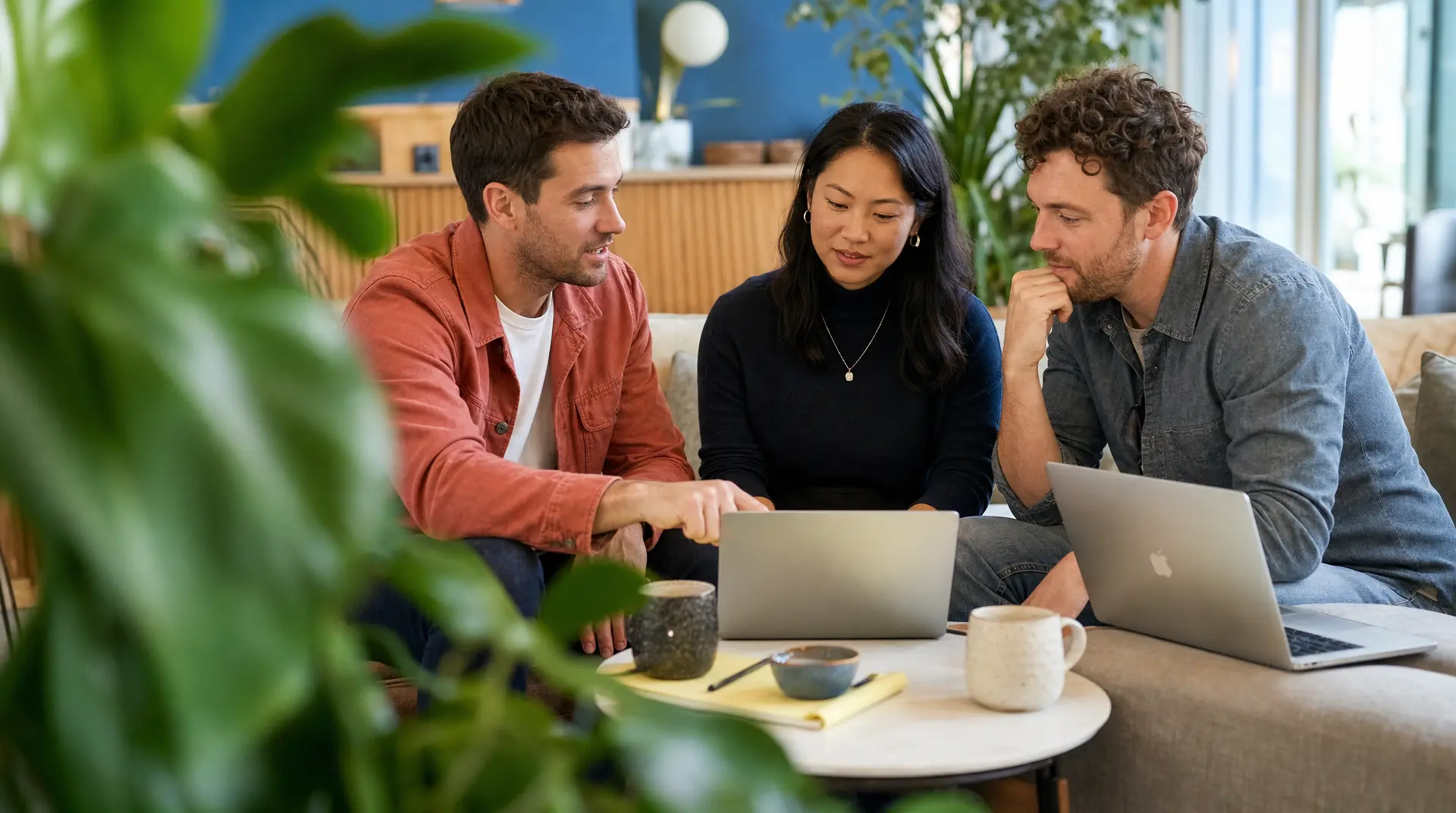 Three colleagues reviewing laptops during talent acquisition planning in a bright office meeting.