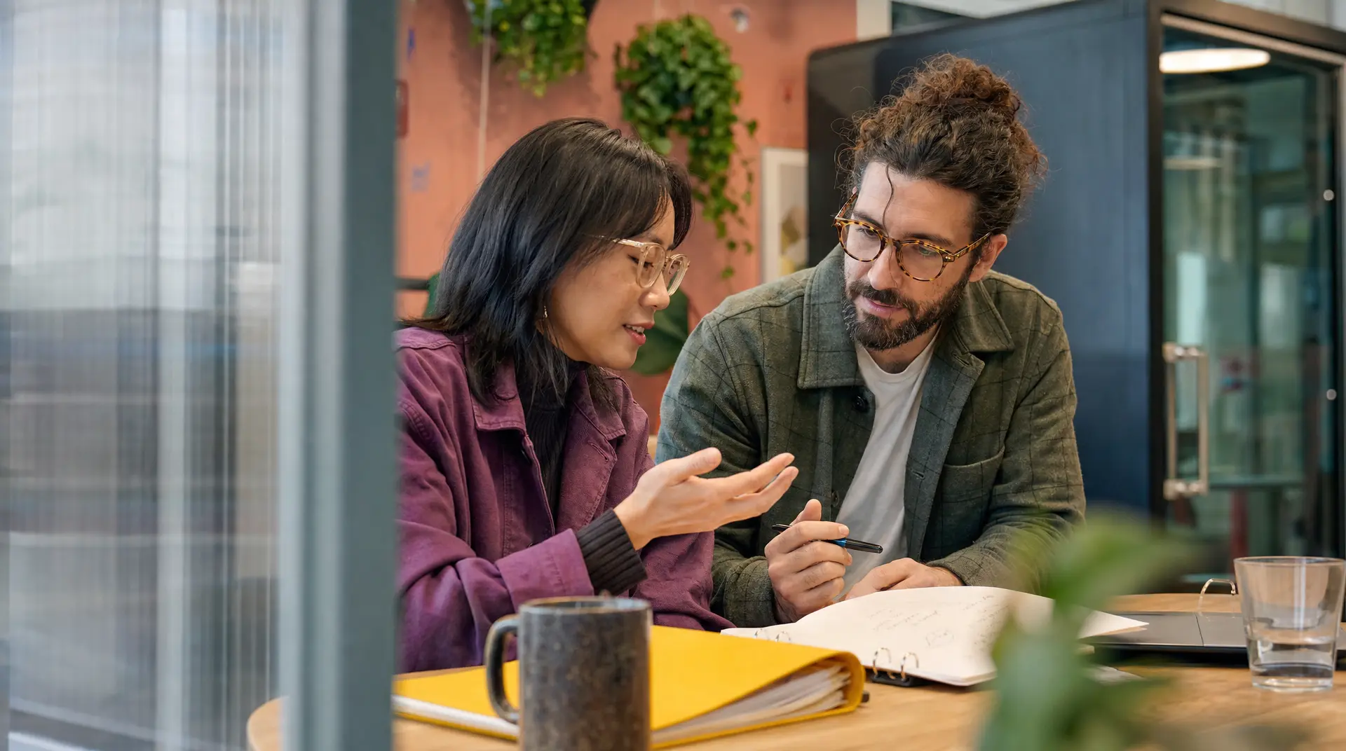 Two professionals discuss notes at a meeting table, supporting recruitment process and candidate experience.