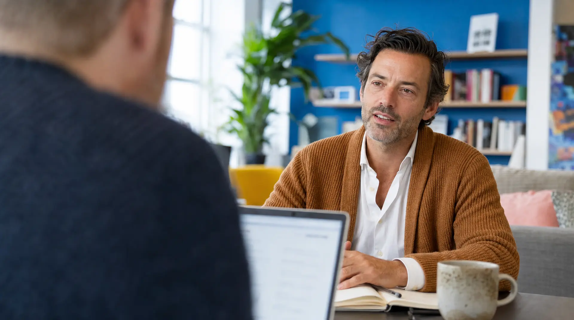 A recruitment consultant meets a candidate in a bright office while an AI for recruitment screen is visible on a laptop in the foreground.