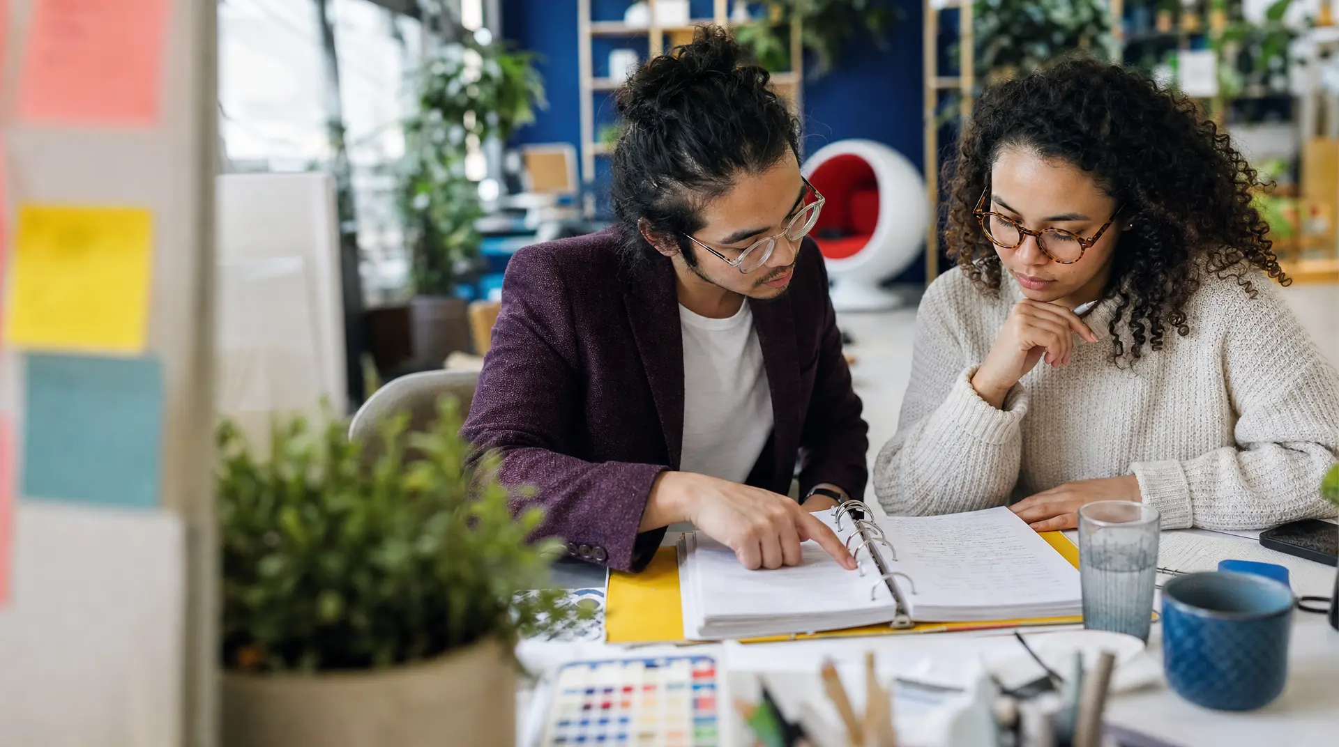 Two professionals review documents at a desk while planning recruitment process outsourcing, with notebooks and a phone nearby.