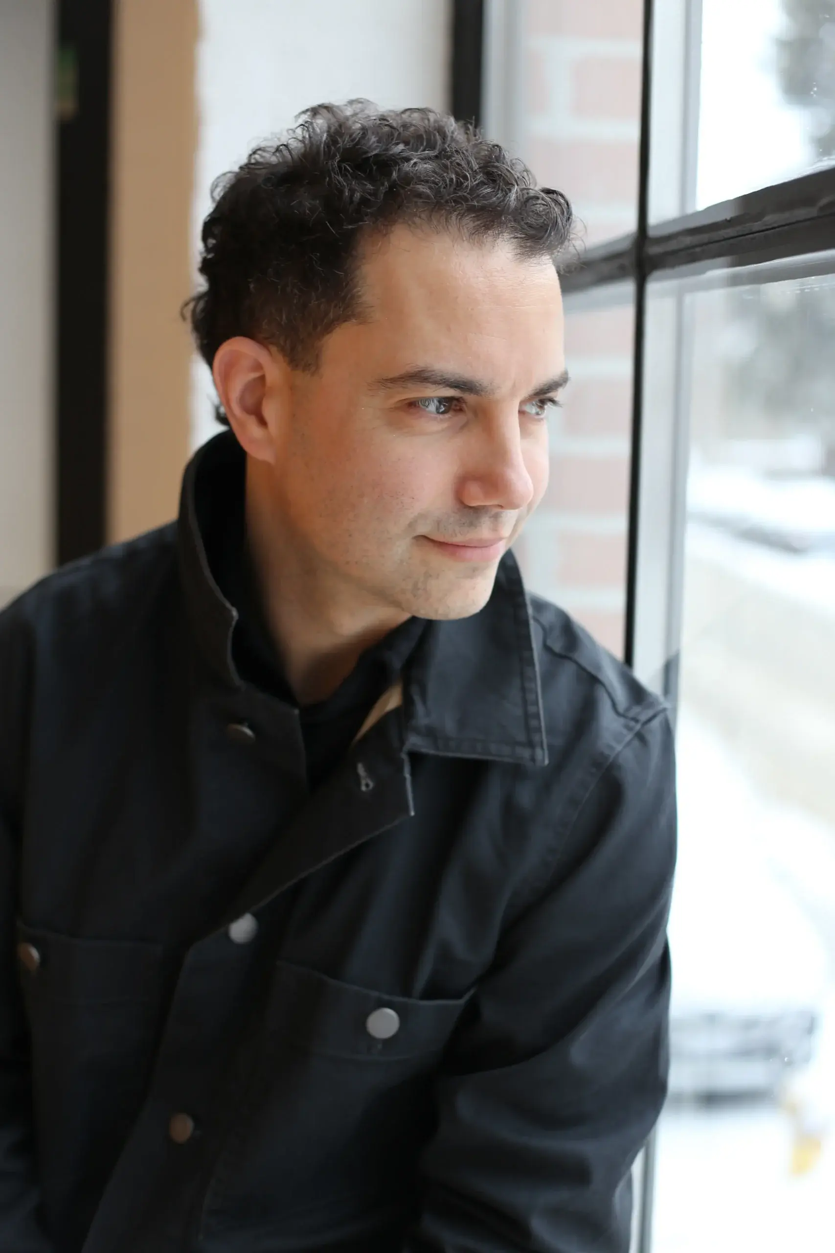 Professional seated near a window, looking thoughtful during a recruitment process conversation.