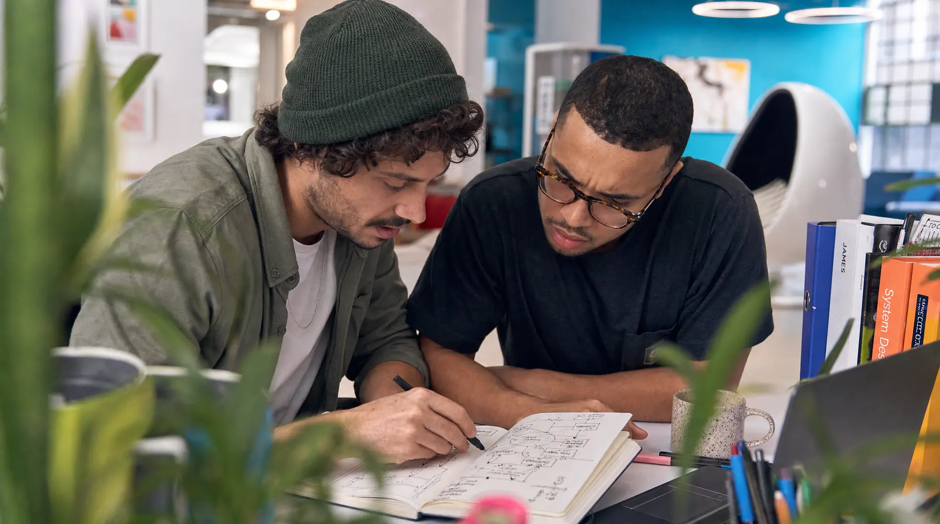 Two coworkers review a whiteboard diagram at a desk, reflecting talent acquisition collaboration in technology recruitment.