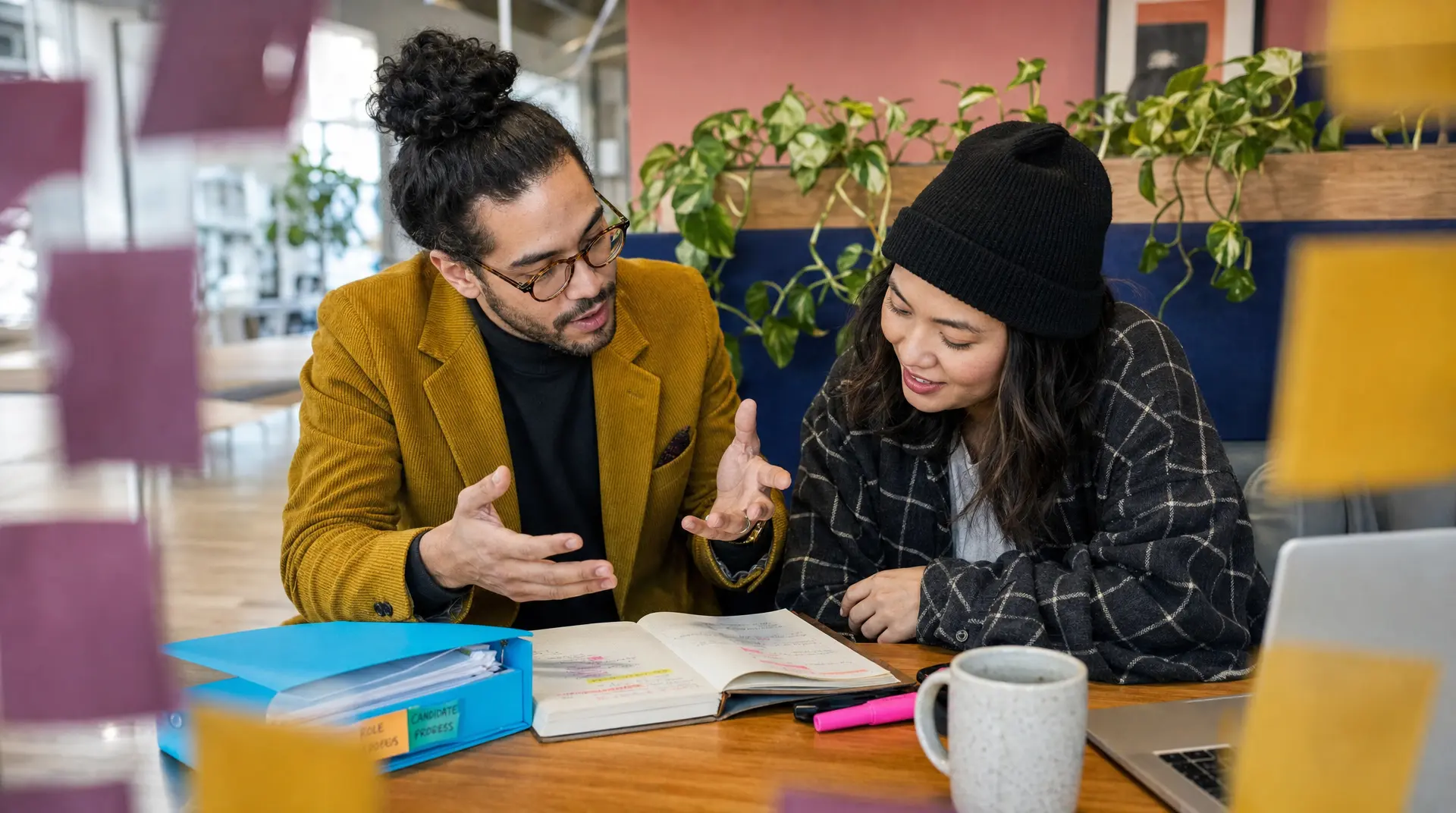 Two recruiters discuss candidate papers at a desk, guiding talent acquisition in the recruitment process.