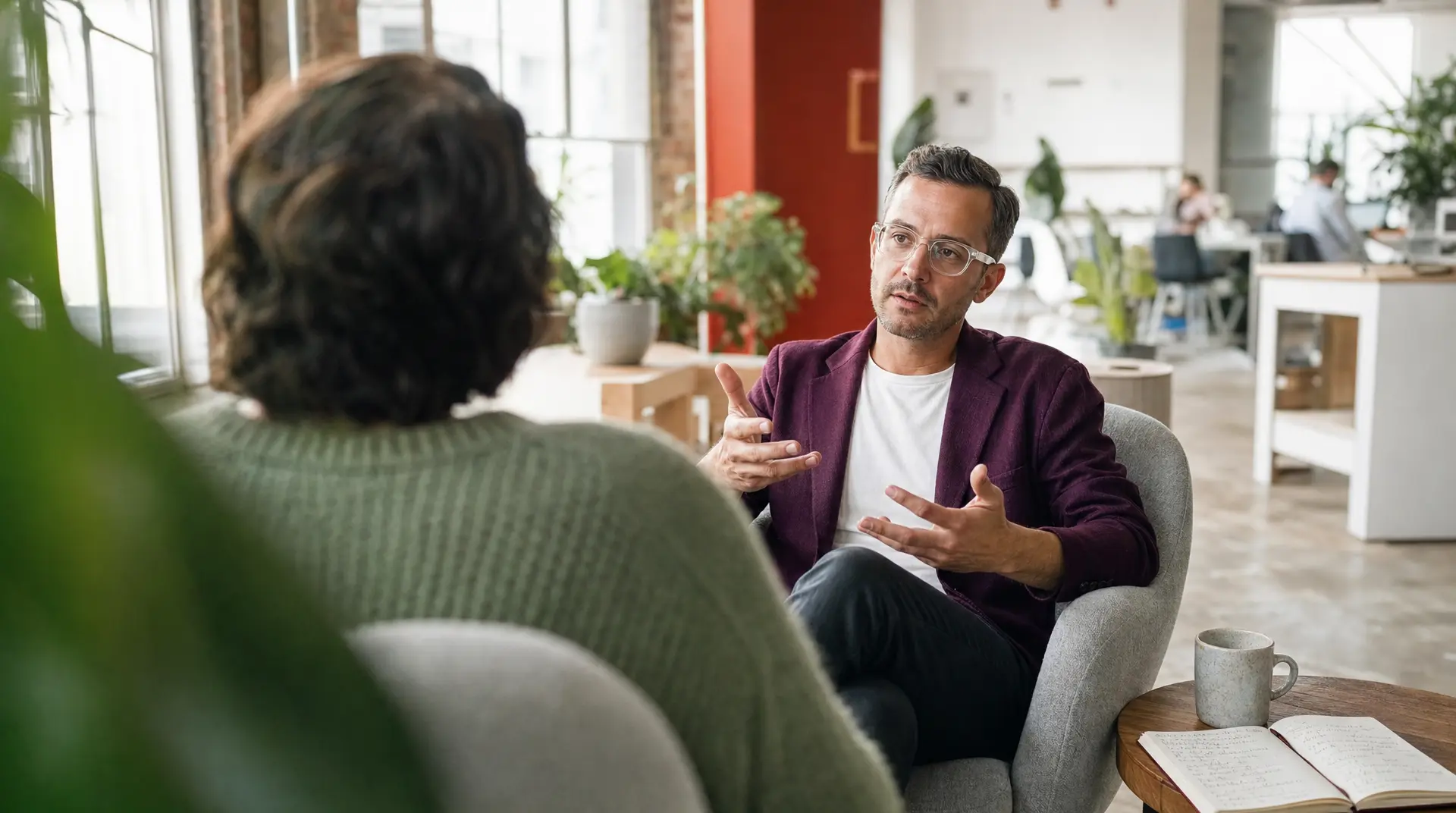 Manager and candidate sit in a relaxed office interview, discussing the recruitment process across an open workspace