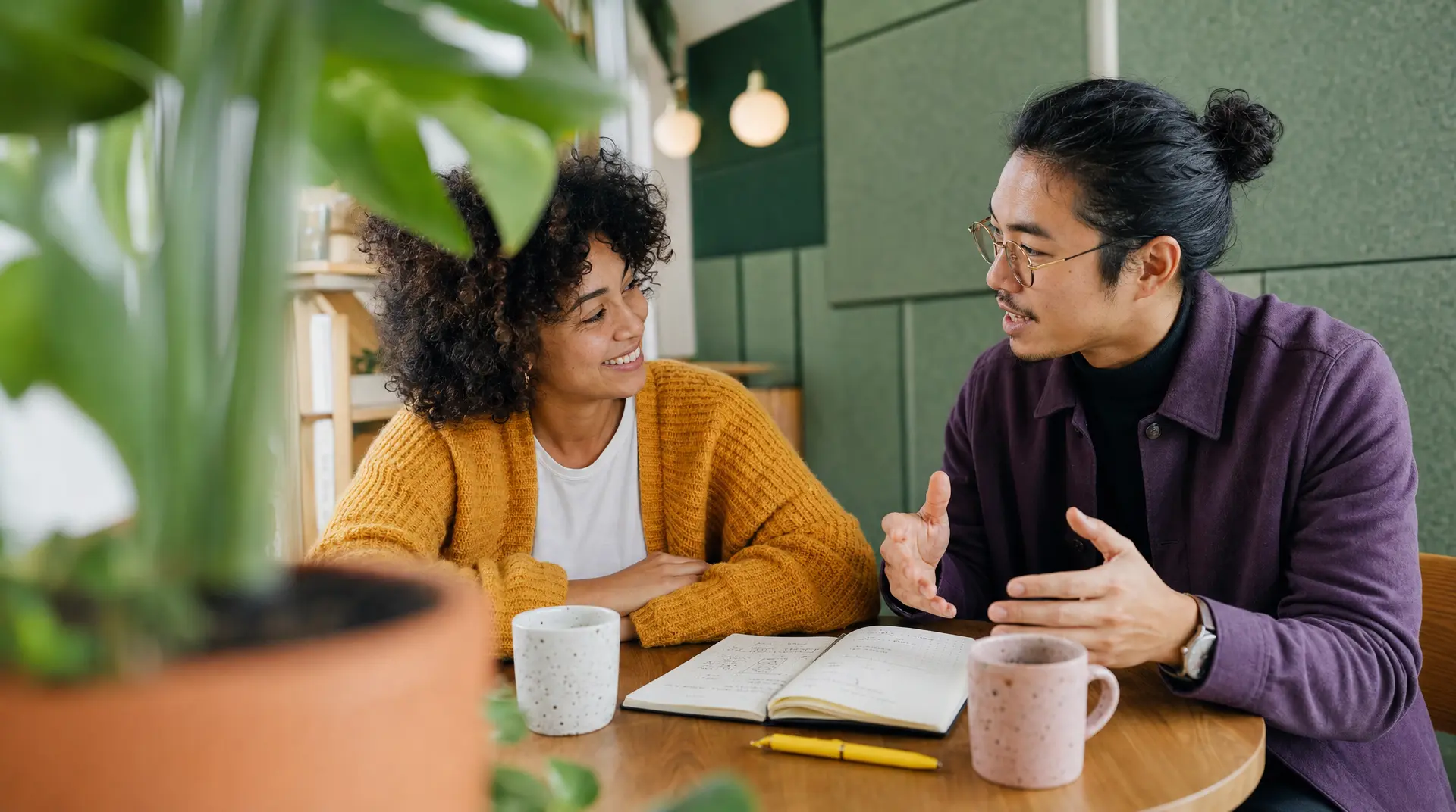 Two professionals sit at a cafe table, discussing an open notebook as part of the recruitment process for talent acquisition.