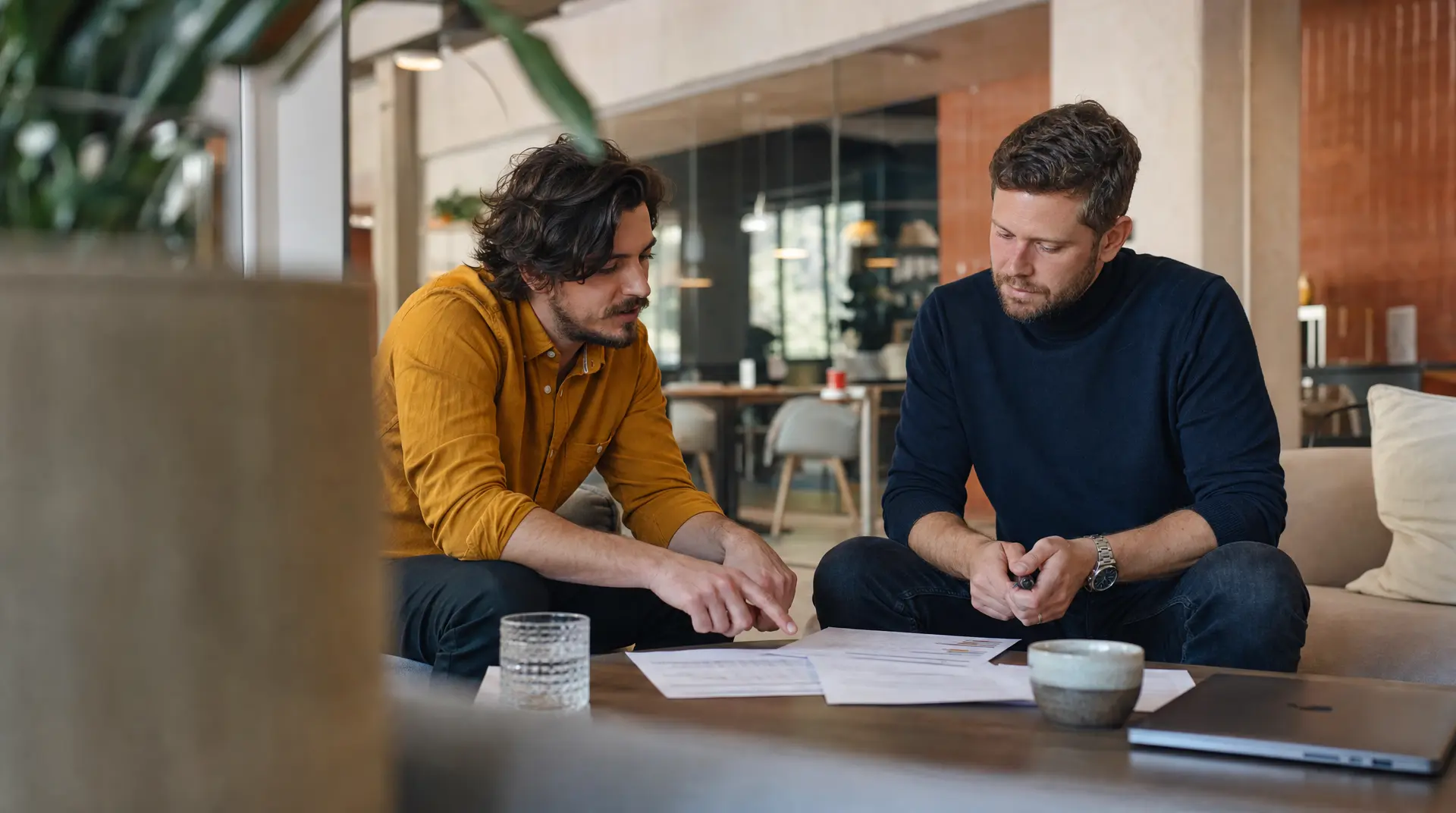 Two professionals sit at a desk reviewing printed documents in an office setting, focused on the recruitment process.